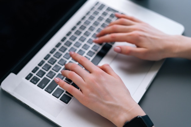 Nahaufnahmehände von nicht erkennbaren Geschäftsfrauen, die auf der Laptop-Notebook-Tastatur tippen, die am Schreibtisch auf dem Hintergrund des Fensters im dunklen Büroraum sitzt, selektiver Fokus.