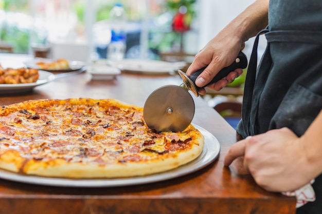 Nahaufnahmehand der Chefausschnittpizza auf Tabelle.