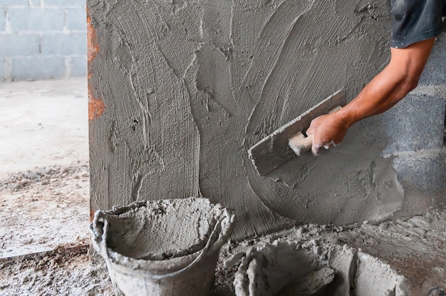 Foto nahaufnahmehand des arbeiters, der zement an der wand in der baustelle verputzt