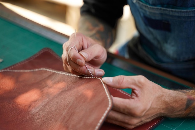 Nahaufnahmehand des Lederhandwerkers ist sorgfältig, eine Ledertasche für einen Kunden zu nähen