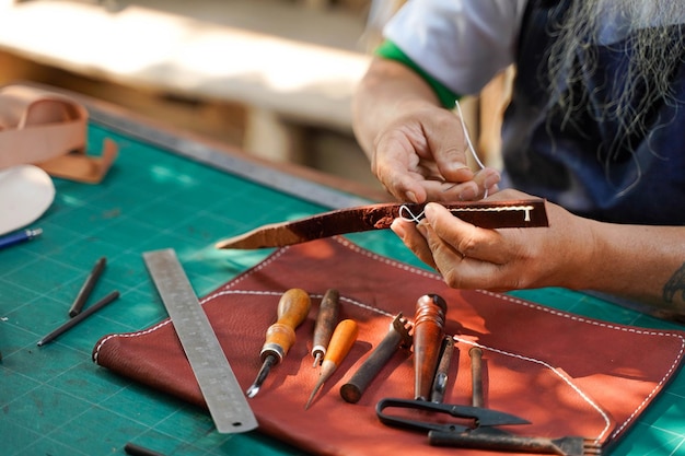 Nahaufnahmehand des Lederhandwerkers ist sorgfältig, einen Ledergürtel für einen Kunden zu nähen