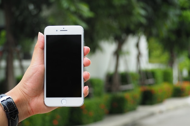 Nahaufnahmehand, die den leeren schwarzen Bildschirm des Smartphone im Freien auf undeutlichem Naturhintergrund zeigt.