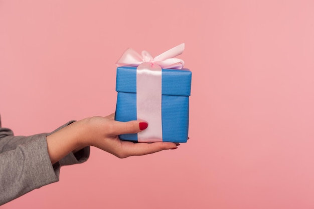 Nahaufnahmehand, die elegante blaue Geschenkbox mit Band, romantische Überraschung für Valentinstag, Weihnachtsfeiertagstradition hält, um Geschenk, Jahrestag oder Geburtstagsfeier zu geben. Studioaufnahme isoliert