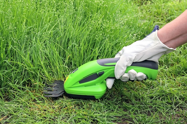 Nahaufnahmehand hält einen elektrischen manuellen Rasentrimmer