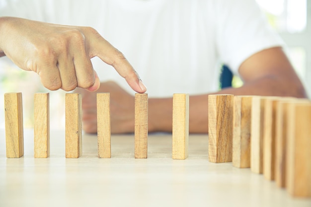 Nahaufnahmehand verhindert, dass Holzblock nicht herunterfällt Dominokonzepte des Finanzrisikomanagements und der strategischen Planung und des Plans für geschäftliche Herausforderungen