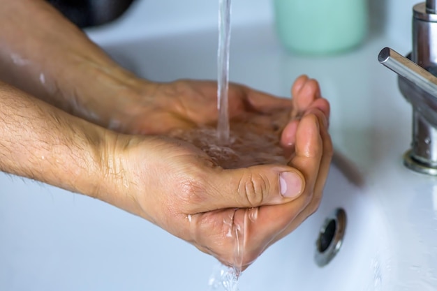 Nahaufnahmemann wäscht seine Hände, Wasser aus dem Wasserhahn gießt auf die Hände des Mannes