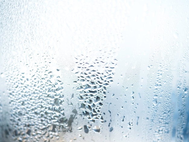 Nahaufnahmenaturwassertropfenbeschaffenheit auf Glas mit unscharfem blauem Hintergrund. Feuchtigkeit der Luft verursacht Dampf auf dem Glas.