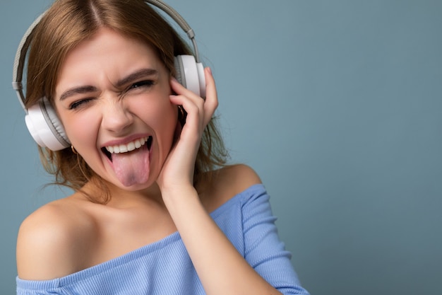 Nahaufnahmeporträt der attraktiven emotionalen jungen blonden Frau, die blaue Erntespitze lokalisiert auf Blau trägt