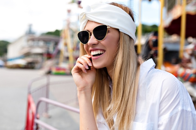 Nahaufnahmeporträt der attraktiven hübschen glücklichen Frau mit den blonden Haaren und dem wunderbaren Lächeln, das an der Kamera in der Stadt aufwirft. junge schöne Hipster Frauen, Streetstyle, glücklich