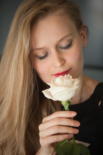 Nahaufnahmeporträt der Frau im schwarzen Kleid mit weißer rosafarbener Blume (Fokus auf den Lippen)