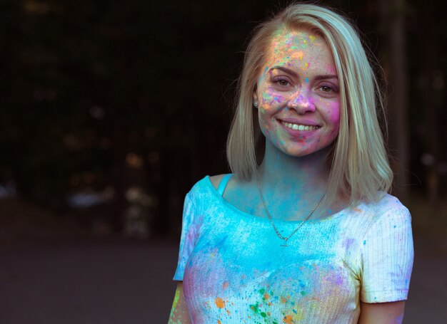 Nahaufnahmeporträt der glücklichen blonden Frau im weißen T-Shirt mit Farbfarbe bedeckte ihr Gesicht beim Holi-Festival. Platz für Text