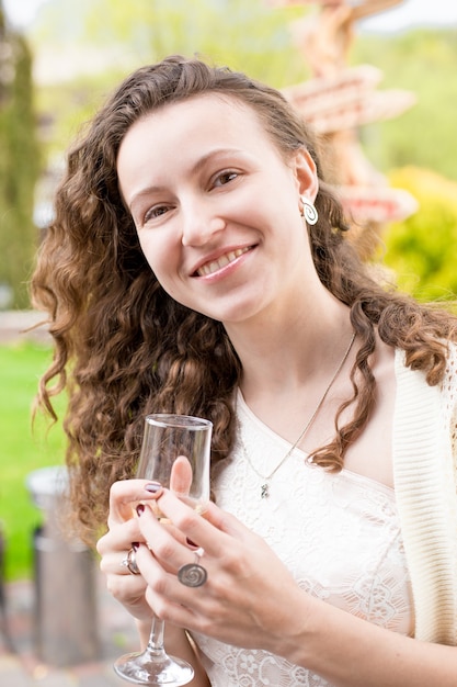 Nahaufnahmeporträt der glücklichen lockigen Frau, die im Park mit Champagner aufwirft