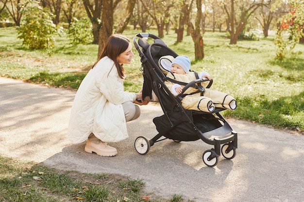 Nahaufnahmeporträt der jungen Frau im Gespräch mit ihrem neugeborenen Sohn im Kinderwagen.