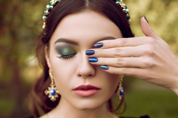 Nahaufnahmeporträt der jungen Frau mit hellblauem Make-up und blauer Maniküre, blaue Dekoration. Make-up und Maniküre im gleichen Stil. Schönheit, Mode, Make-up, Maniküre.