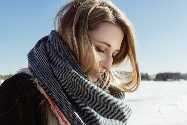 Nahaufnahmeporträt der jungen weißen erwachsenen Frau in einem Schal auf einem gefrorenen Fluss, selektiver Fokus