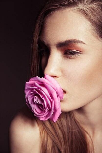 Nahaufnahmeporträt der schönen brünetten Frau mit rosa Rose