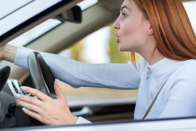 Nahaufnahmeporträt der verärgerten verärgerten wütenden aggressiven Frau, die ein Auto fährt, das jemanden mit der Handfaust nach oben schreit. Negativer menschlicher Ausdruck.