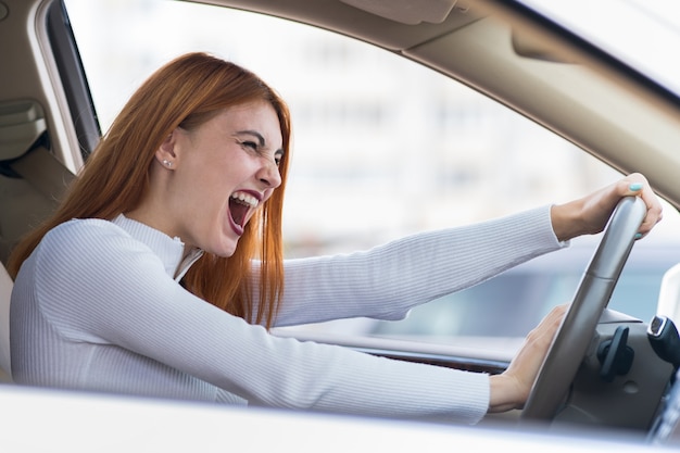 Nahaufnahmeporträt der verärgerten verärgerten wütenden aggressiven Frau, die ein Auto fährt, das jemanden mit der Handfaust nach oben schreit. Negativer menschlicher Ausdruck.