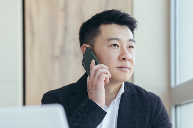 Nahaufnahmeporträt des asiatischen Geschäftsmannes, erfolgreiches und ernstes Telefongespräch, in einem Geschäftsanzug