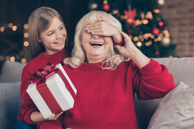 Nahaufnahmeporträt des Enkels, das Omas Augen schließt, die Geschenk an verziertem Innenhaus geben