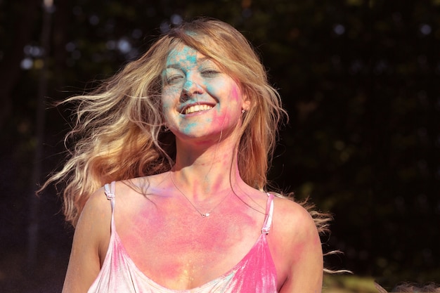 Nahaufnahmeporträt des erfreuten jungen Modells mit Wind im Haar, das auf Holi-Festival aufwirft