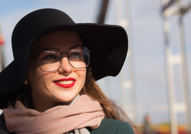 Nahaufnahmeporträt des erstaunlichen jungen Modells, das an der Brücke aufwirft. Frau mit modischem Hut, Schal und Brille