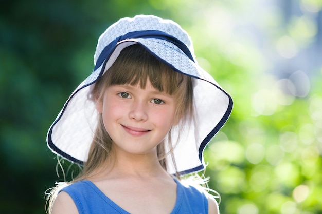Nahaufnahmeporträt des glücklichen lächelnden kleinen Mädchens in einem großen Hut. Kind, das Spaßzeit draußen im Sommer hat.