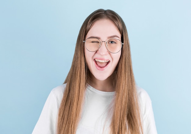 Nahaufnahmeporträt des jungen europäischen Mädchens. Glückliche Frau mit lächelndem Gesicht, das auf Blau blinkt