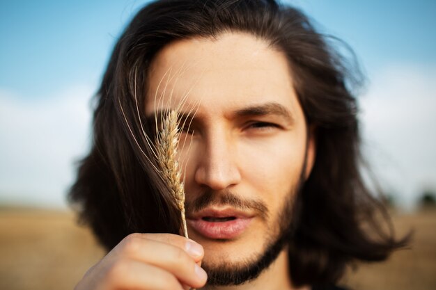 Nahaufnahmeporträt des jungen gutaussehenden Mannes mit dem langen Haar. Weizenspitze halten.