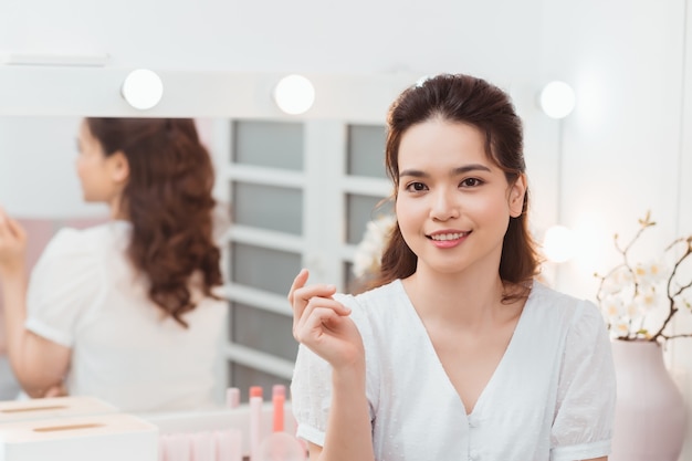 Nahaufnahmeporträt des jungen schönen asiatischen Mädchens mit Spiegel für Make-up-Routine mit Kopienraum.