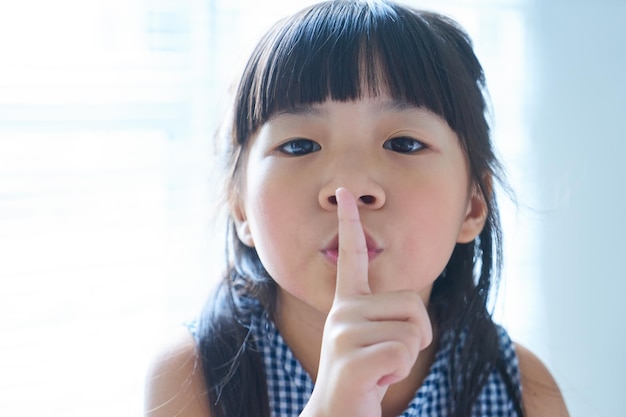 Nahaufnahmeporträt des kleinen asiatischen chinesischen Mädchens, das ihren Finger in einer Geste für Stille an ihre Lippen hält