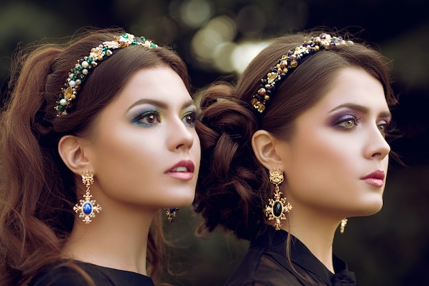 Nahaufnahmeporträt des Lebensbildes von zwei jungen schönen Frauen. Nervöser, stilvoller Schmuck, modisches, trendiges Make-up, goldene Ohrringe mit Steinen Reifen auf dem Kopf mit Edelsteinen.