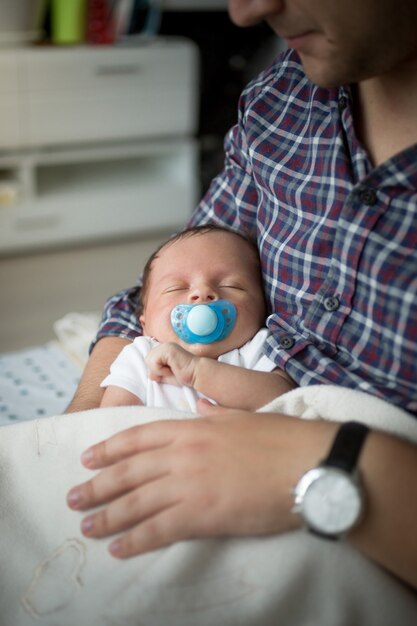 Nahaufnahmeporträt des netten Babys schlief auf den Händen des Vaters ein