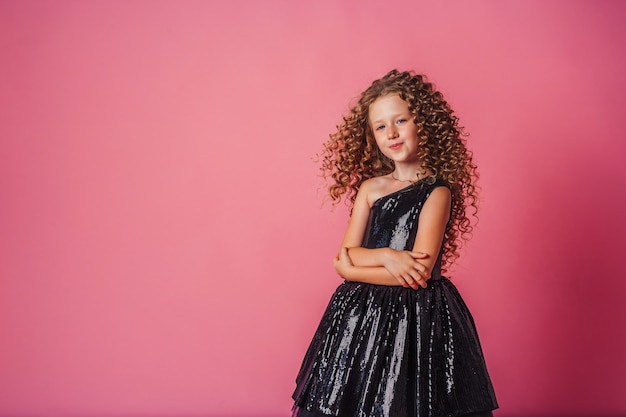 Nahaufnahmeporträt des schönen Mädchens im schwarzen Kleid auf rosa Hintergrund im Studio, das lächelt und posiert