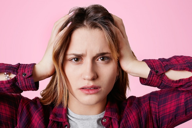 Nahaufnahmeporträt des stressigen weiblichen Modells berührt Kopf und leidet unter Kopfschmerzen, sieht frustriert aus