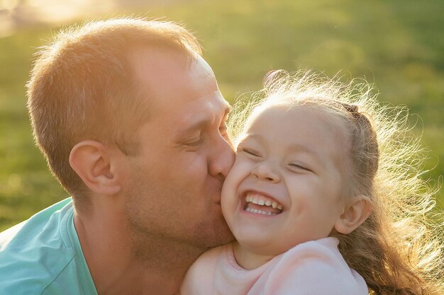Nahaufnahmeporträt des Vaters, der im Sommerpark ein glückliches kleines Mädchen auf die Wange küsst