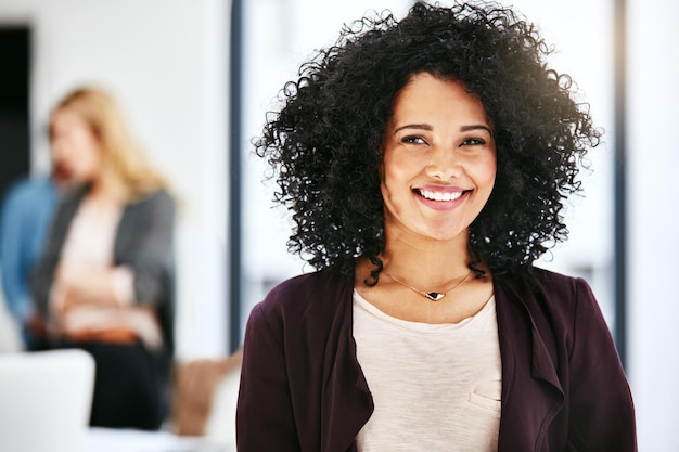 Nahaufnahmeporträt einer glücklichen erfolgreichen und selbstbewussten Geschäftsfrau, die in einem Büro steht Schöne afroamerikanische Frau, die mit ihren Kollegen im verschwommenen Copyspace-Hintergrund lächelt