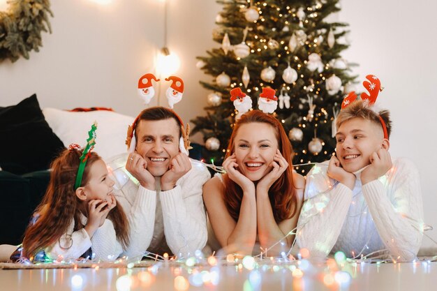 Nahaufnahmeporträt einer glücklichen Familie, die nahe einem Weihnachtsbaum liegt und einen Feiertag feiert.