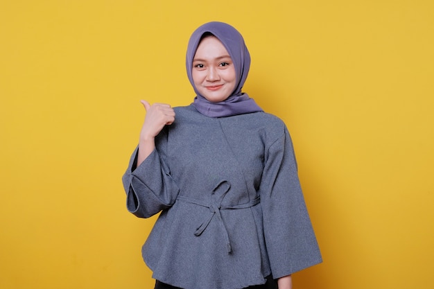 Nahaufnahmeporträt einer glücklichen jungen asiatischen frau, die hijab trägt, die geste mit dem daumen nach oben zeigt