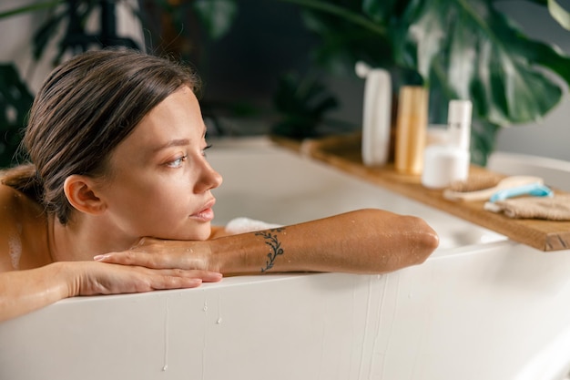 Nahaufnahmeporträt einer hübschen jungen Frau, die beim Entspannen in der Badewanne im luxuriösen Spa-Resort beiseite schaut