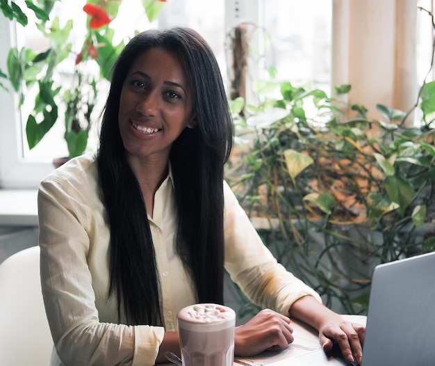 Nahaufnahmeporträt einer jungen Afrikanerin, die sich im Café mit Laptop entspannt und einen Anruf tätigt, Lebensstil und Personenkonzept