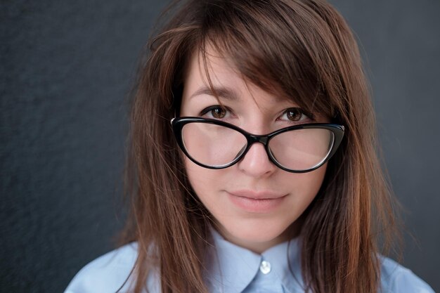 Nahaufnahmeporträt einer jungen attraktiven Frau mit Brille auf dunklem Hintergrund