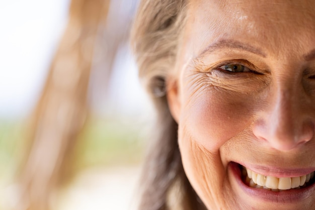 Nahaufnahmeporträt einer kaukasischen Seniorin mit braunen Augen, die lächelt und in die Kamera blickt. Kopierraum, unverändert, Ruhestand, Urlaub, Vergnügen, Strand, Gesicht, Glück und Lifestyle-Konzept.