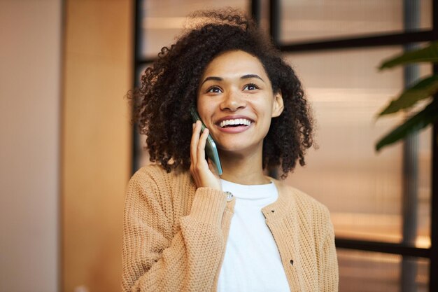 Nahaufnahmeporträt einer schönen lächelnden afroamerikanischen Frau, die auf Handy spricht