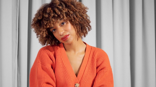 Nahaufnahmeporträt einer schwarzen Mischlingsfrau mit strukturiertem, lockigem Afro-Haar in leuchtend orangefarbener Jacke mit natürlichem Make-up für dunkle Hauttöne