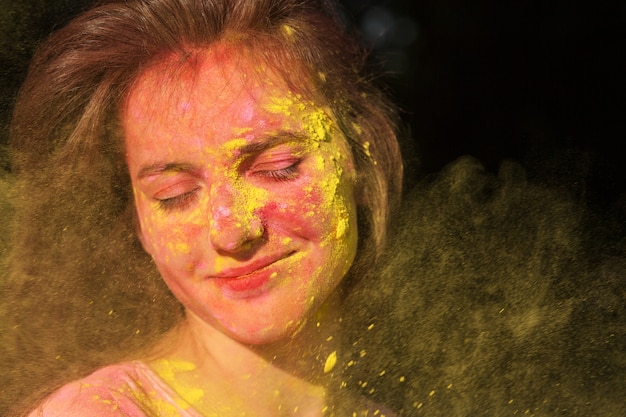 Nahaufnahmeporträt einer wunderbaren brünetten Frau mit Holi-Farbe, die ihr ins Gesicht weht