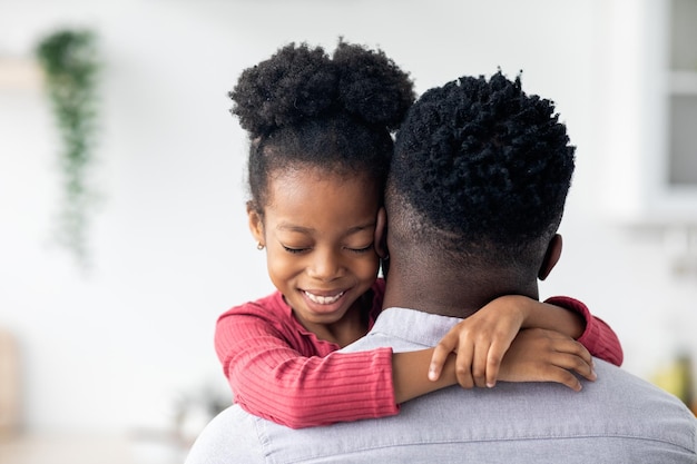 Nahaufnahmeporträt eines afroamerikanischen kleinen Mädchens, das ihren Vater umarmt