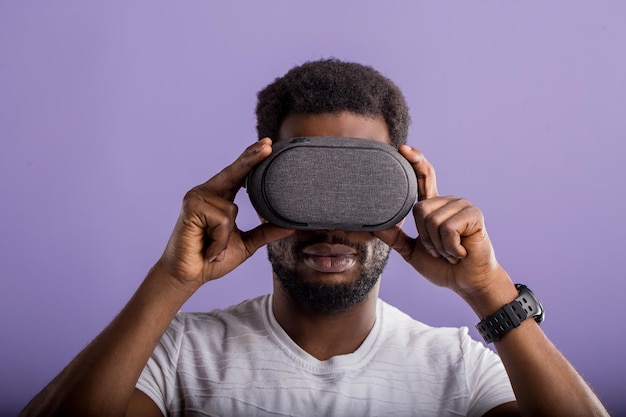 Nahaufnahmeporträt eines afroamerikanischen Mannes, der eine VR-Brille trägt, über virtuelles Projekt arbeitet, neue Realität genießt, Videospiel spielt und isoliert gegen violette Wand posiert. Technologie, Innovations-Gadgets.