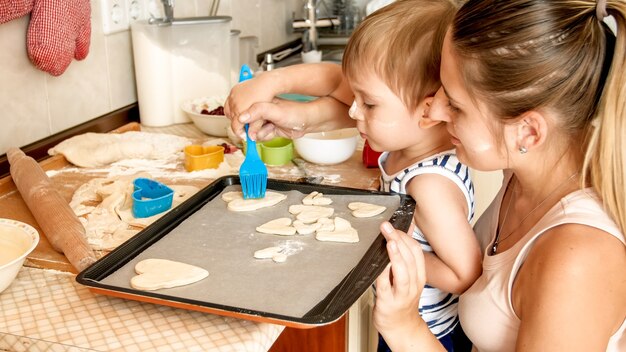 Foto nahaufnahmeporträt eines entzückenden 3 jahre alten kleinkindjungen, der kekse mit mutter macht