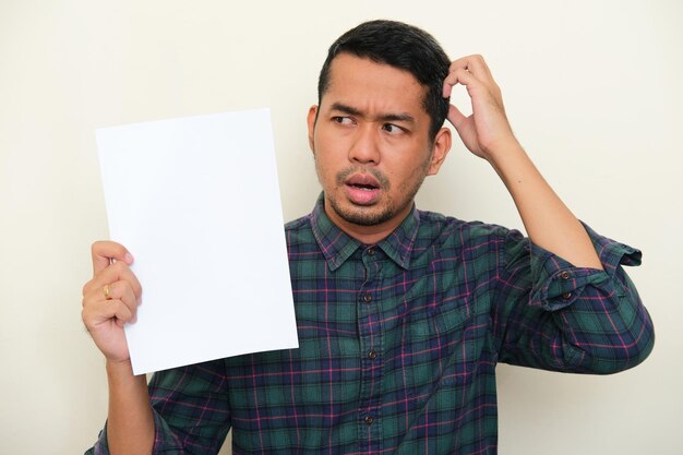 Nahaufnahmeporträt eines erwachsenen asiatischen Mannes, der leeres weißes Papier mit verwirrtem Ausdruck zeigt